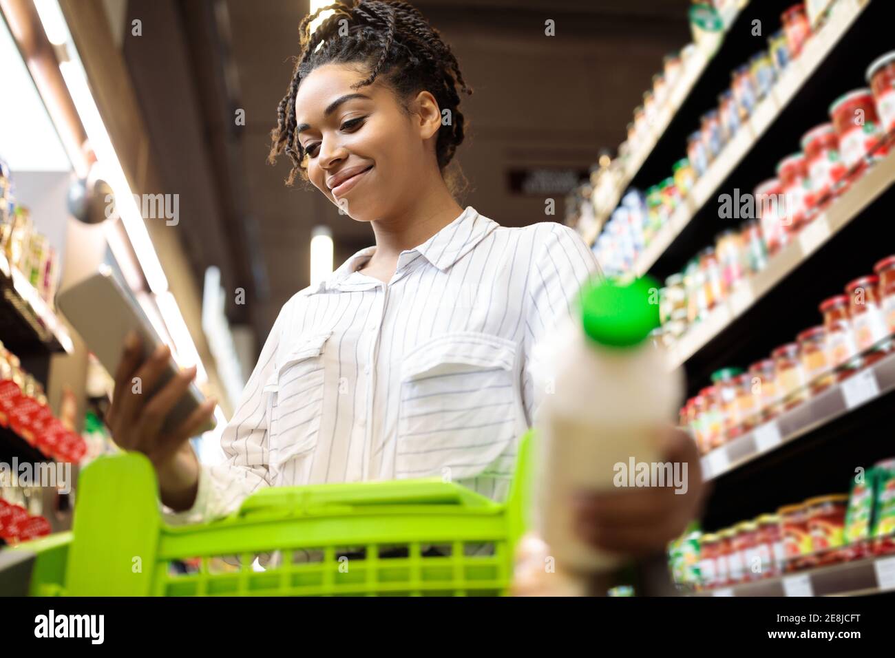Femme afro-américaine utilisant des articles d'épicerie par téléphone dans un supermarché Banque D'Images
