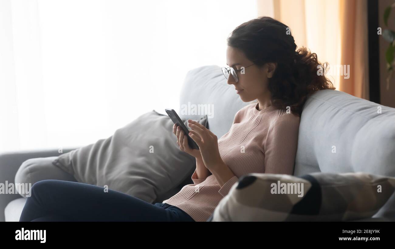Une jeune femme détendue dans des lunettes utilisant des applications mobiles à la maison. Banque D'Images