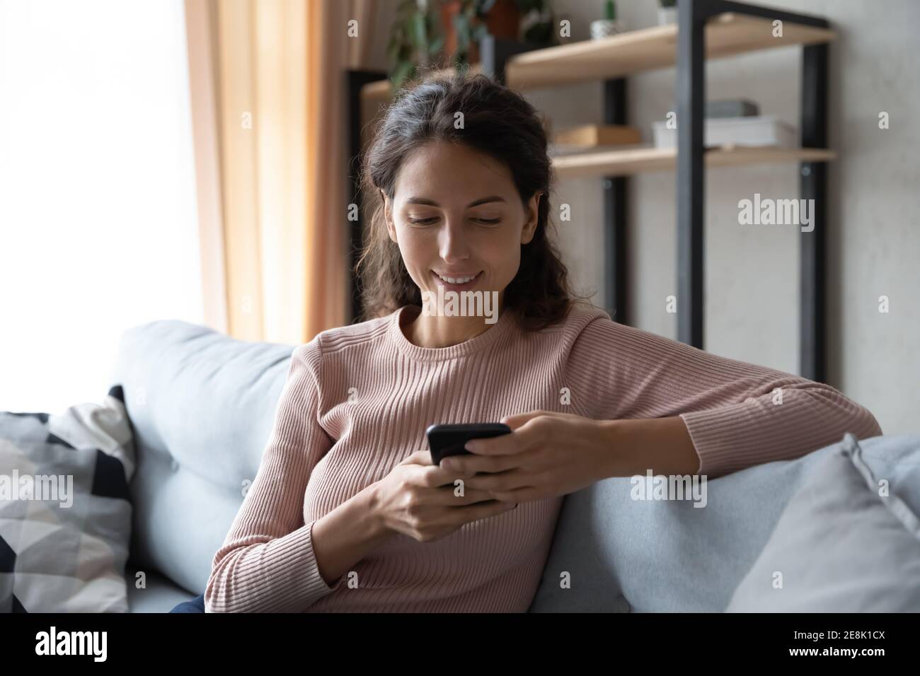 Jeune femme détendue utilisant un smartphone assis sur un canapé. Banque D'Images