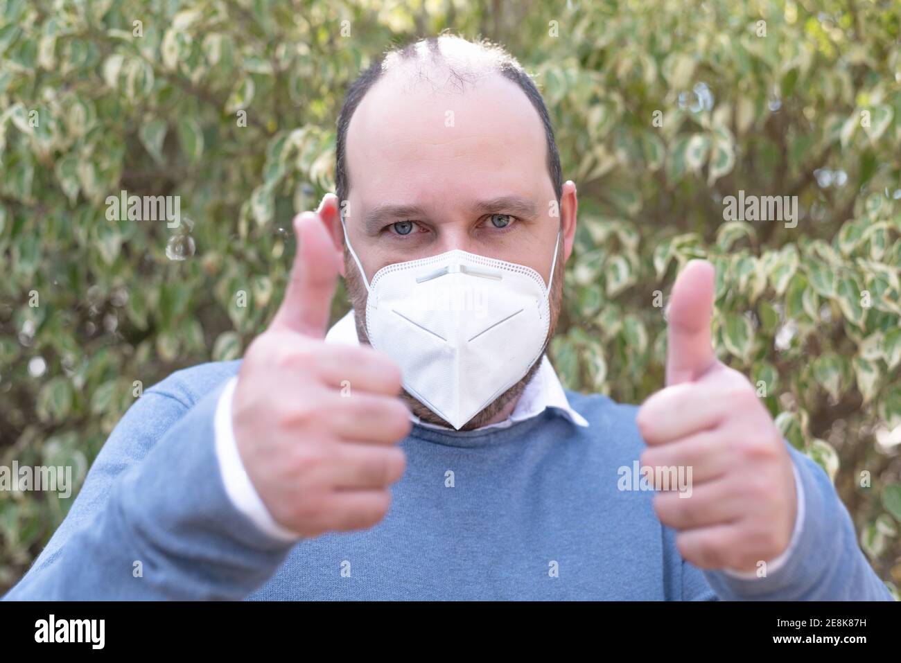 J'aime! Portrait de l'homme beau optimiste avec masque médical en t-shirt bleu montrant les pouces vers le haut geste et sourire, c'est, bien fait, bon travail Banque D'Images