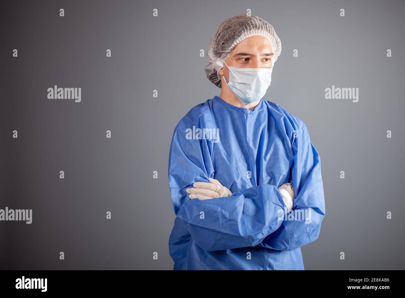 Un beau chirurgien masculin est un médecin sur fond gris dans le studio. Un  homme en robe, un masque médical, un chapeau, des gants. Espace vide pour  le texte. Un homme St