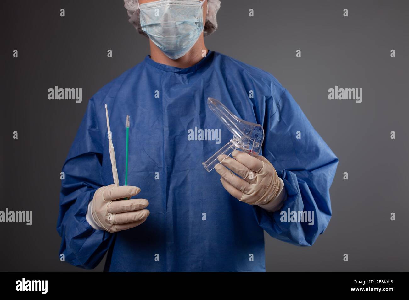 Un gynécologue avec un miroir de vénus entre ses mains. Accessoires  gynécologiques, brosse, bâton. Un médecin dans un masque médical, une robe,  des gants, un chapeau avec un gyn Photo Stock -