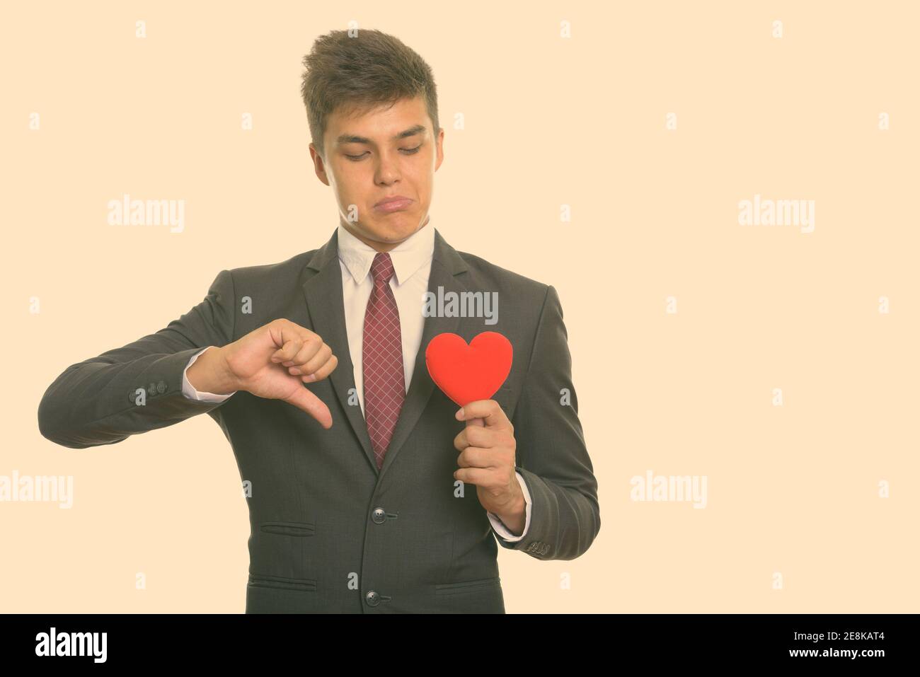 Jeune homme triste giving thumb vers le bas tout en maintenant et à la recherche à cœur rouge prêt pour la Saint-Valentin Banque D'Images