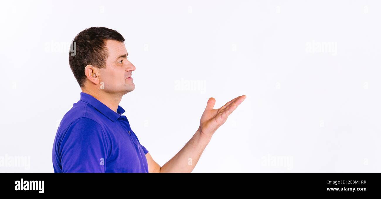 Bannière,format long. Photo de profil. L'homme avec l'aide auditive atteint avec sa main vide et regarde loin. Arrière-plan blanc et espace vide latéral. Banque D'Images