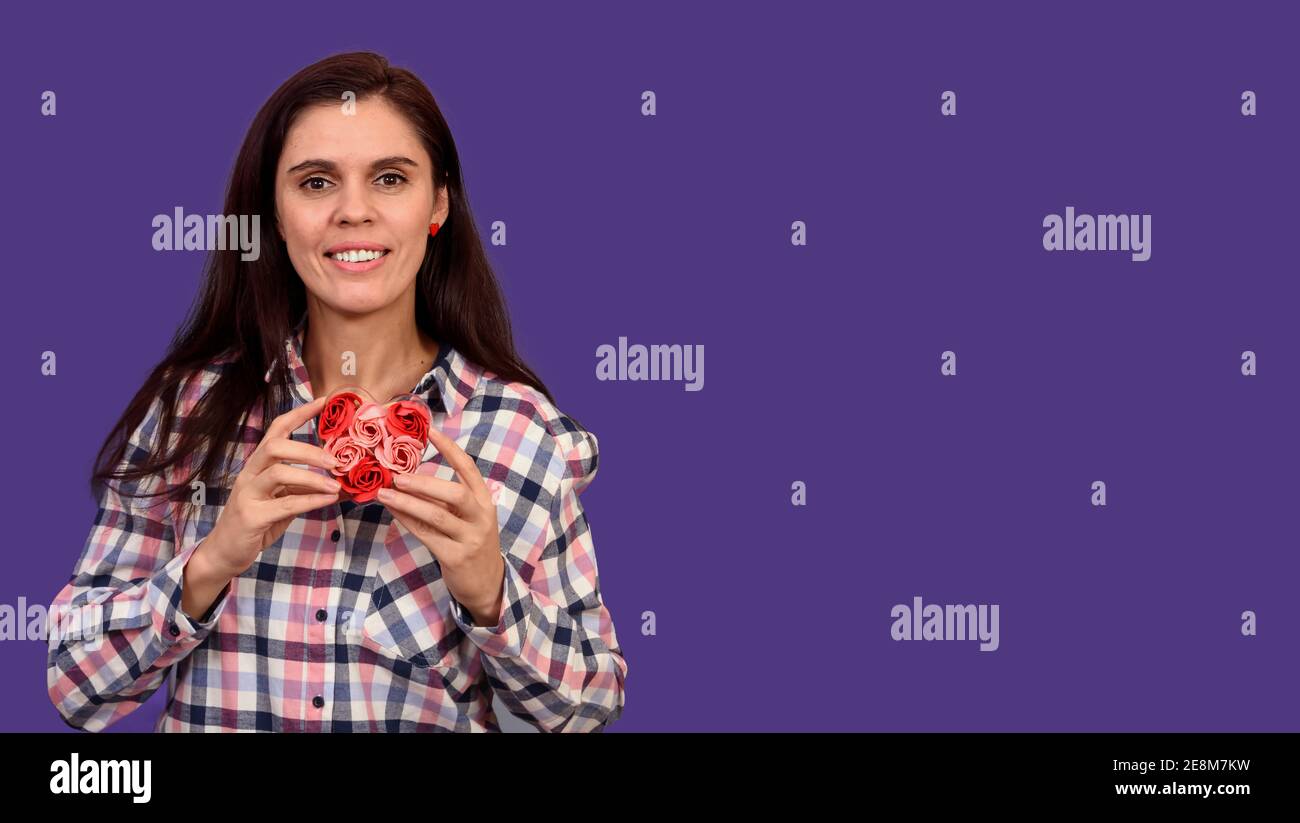 Portrait d'une jolie femme dans une chemise à carreaux tenue un coeur de rose en plastique sur fond lilas Banque D'Images