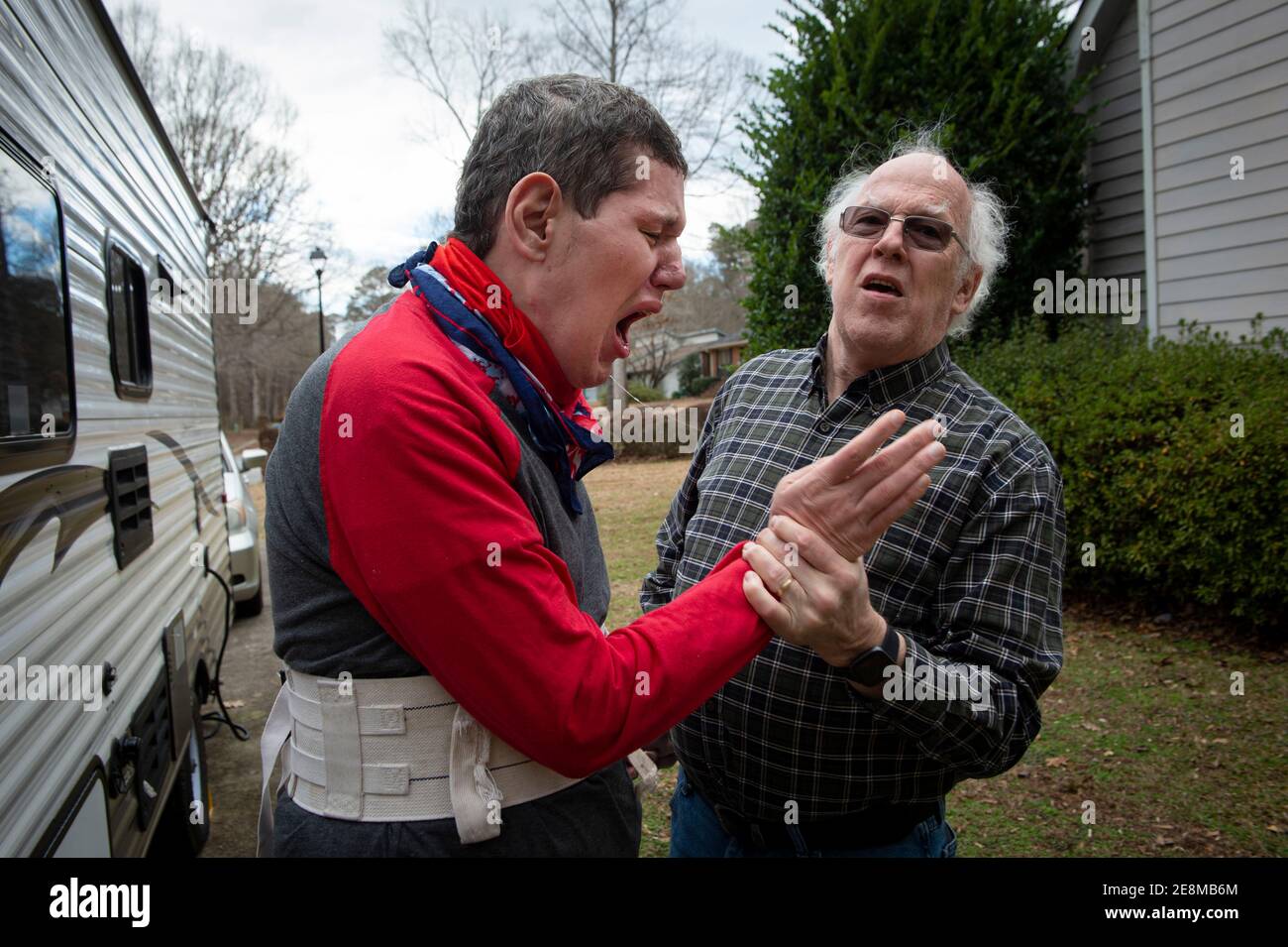 Jonesboro, GA, États-Unis. 31 janvier 2021. Mike McBroom tente d'empêcher son fils handicapé de se blesser lors d'une promenade à l'extérieur de sa maison. Mike et sa femme Sheila sont souvent éveillés la nuit, pleins d'inquiétude quant à l'avenir de Tim's. Tim, 36 ans, qui est non verbal et connaît un autisme grave, a des crises et des problèmes de comportement. McBroom et sa femme font de leur mieux pour offrir à leur fils un environnement sûr et sécuritaire dans leur maison de Jonesboro, avec l'aide quotidienne du personnel de soutien financé par Medicaid. Mais les réductions proposées à ces services financés par Medicaid bouleversent la vie de leur fils s. G Banque D'Images