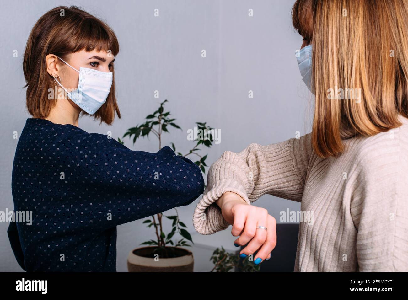 Deux filles masquées au travail saluent leurs coudes. Distanciation sociale. Nouvelle réalité. Concept de vie pendant la pandémie du coronavirus Banque D'Images