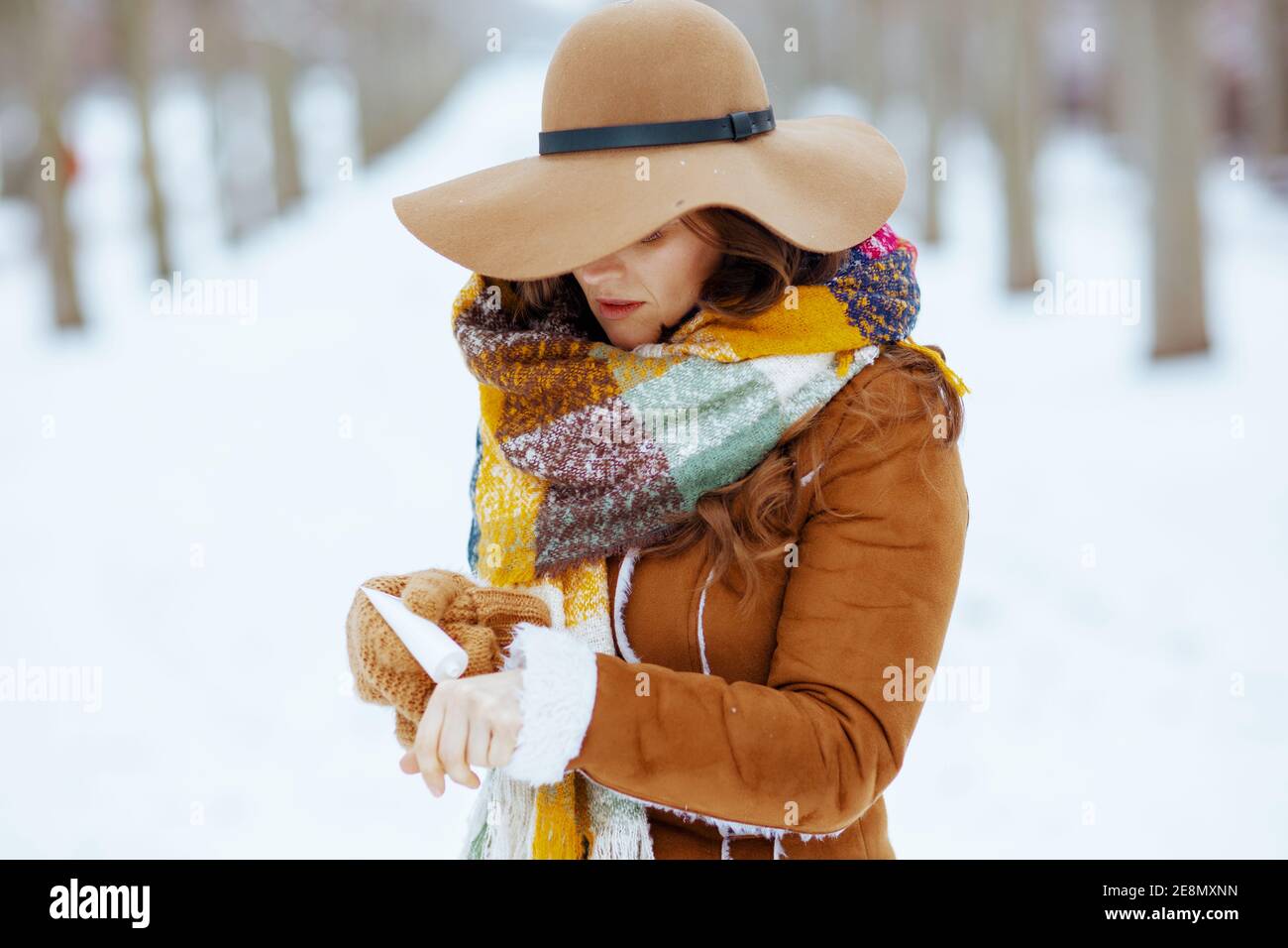 femme moderne en chapeau brun et écharpe avec moufles en peau de mouton en  utilisant la crème pour les mains dehors dans le parc de la ville en hiver  Photo Stock -