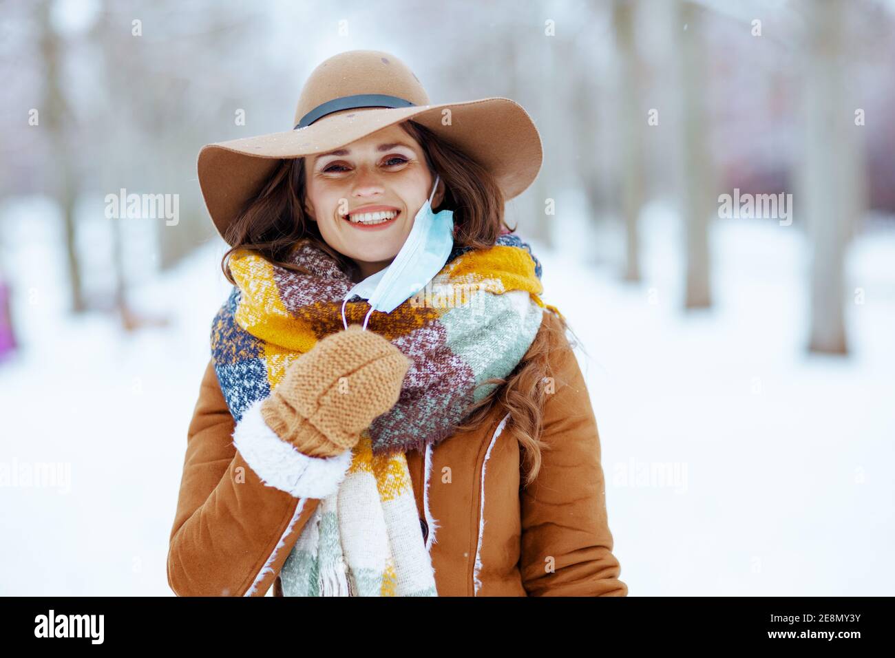 femme moderne souriante en chapeau marron et écharpe avec moufles et masque  médical en peau de mouton à l'extérieur dans le parc de la ville en hiver  Photo Stock - Alamy