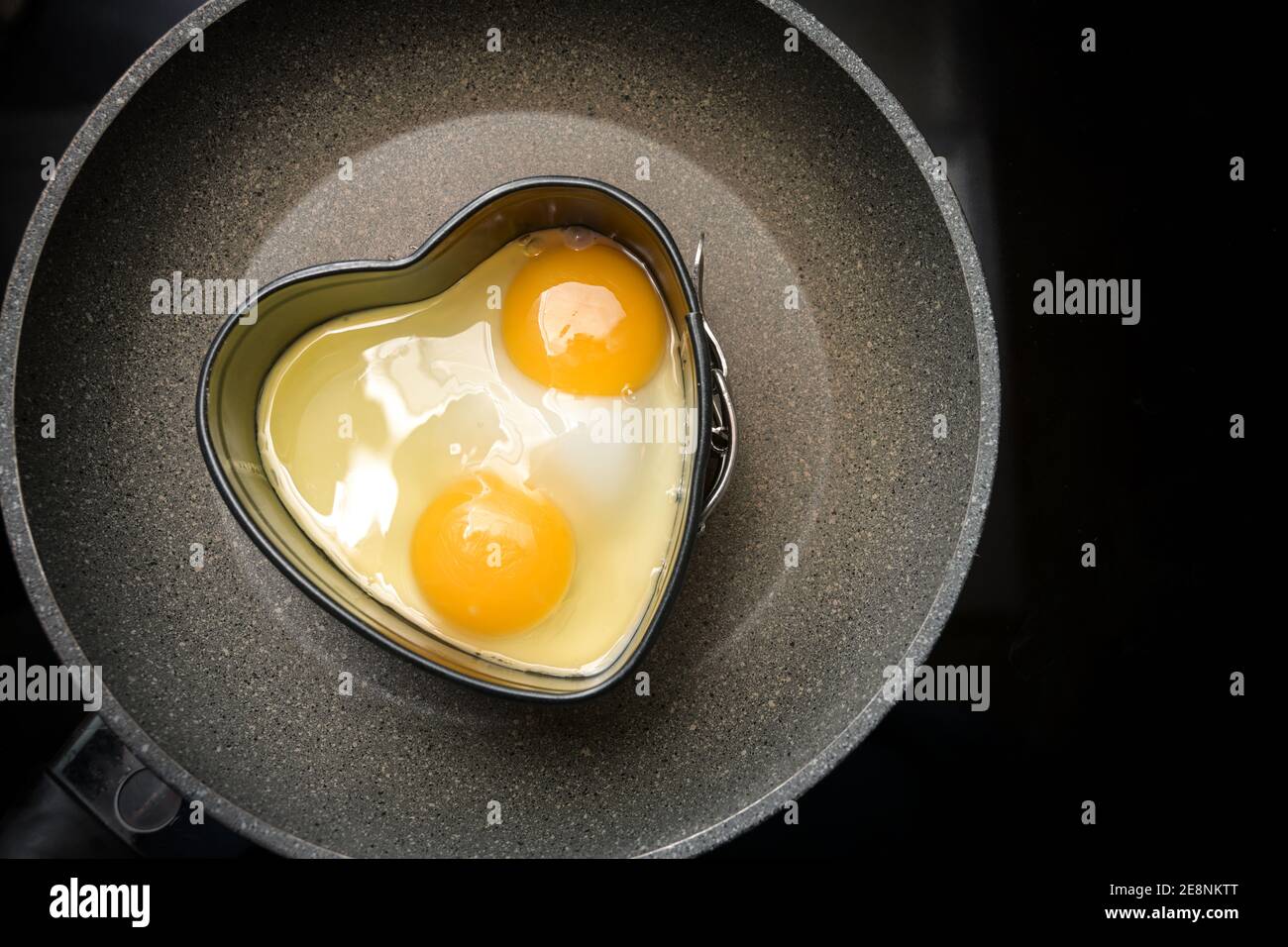 Deux œufs frits en forme de coeur sur une poêle noire, préparation pour un petit déjeuner romantique de jour de Saint Valentin, espace copie, haute vue ange f Banque D'Images