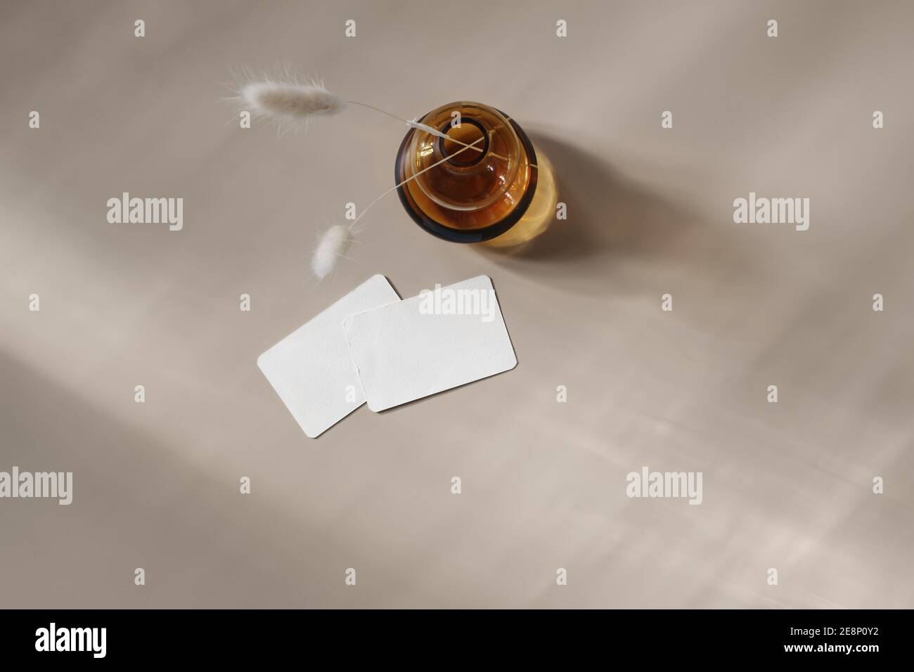 Moderne papeterie d'été encore la vie scène. Vase en verre ambré avec herbe lagurus sèche. Cartes de visite vierges sur fond de table beige au soleil Banque D'Images