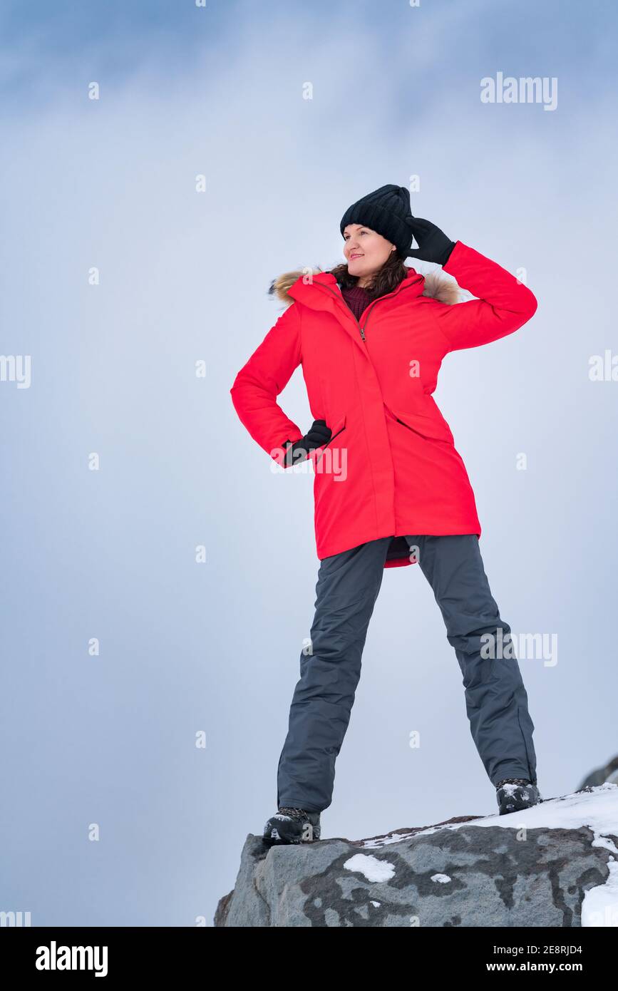 Jeune femme debout sur le sommet de la montagne sur fond de ciel avec des nuages spectaculaires. Femme souriante vêtue d'une veste coupe-vent rouge, d'un pantalon de sport Banque D'Images