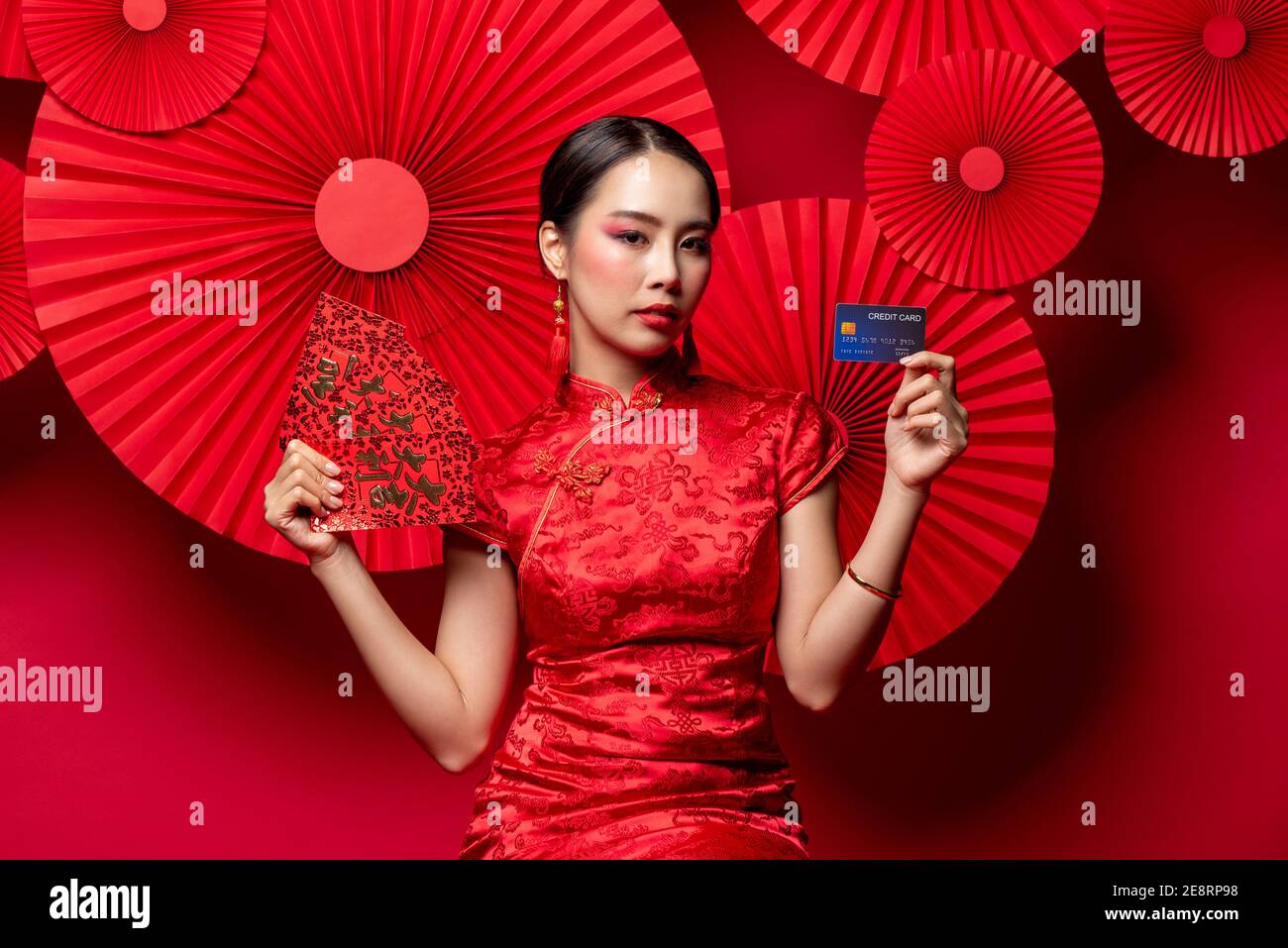 Belle femme asiatique en robe traditionnelle qipao tenant des enveloppes rouges Ou Ang Pao et carte de crédit sur le style oriental de studio Arrière-plan rouge pour Chines Banque D'Images