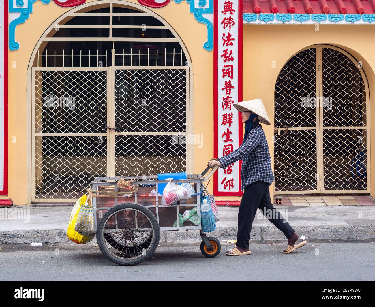 Femme vietnamienne poussant une charrette devant un sanctuaire de Buddhiust à Ho Chi Minh ville, Vietnam. Banque D'Images