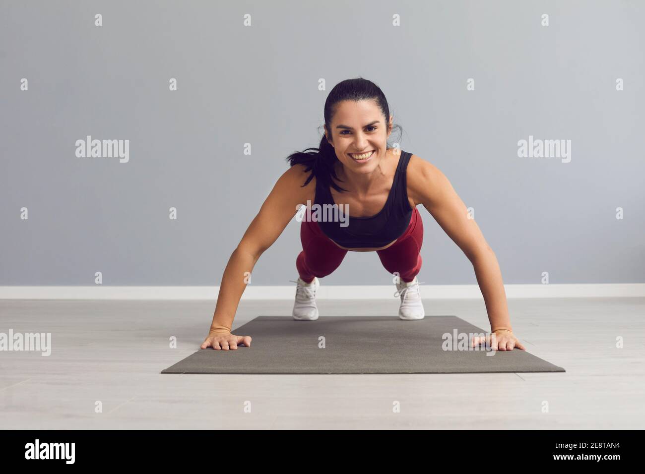 Bonne femme souriante regardant l'appareil photo tout en faisant des push-up sur tapis de sport à la salle de gym Banque D'Images