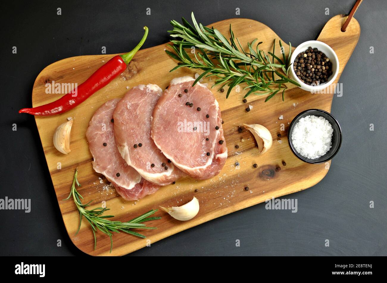 Plat de filet de viande de porc frais non cuite, cru, au romarin, au poivre, au sel, au piment rouge et à l'ail sur bois et fond noir. Banque D'Images