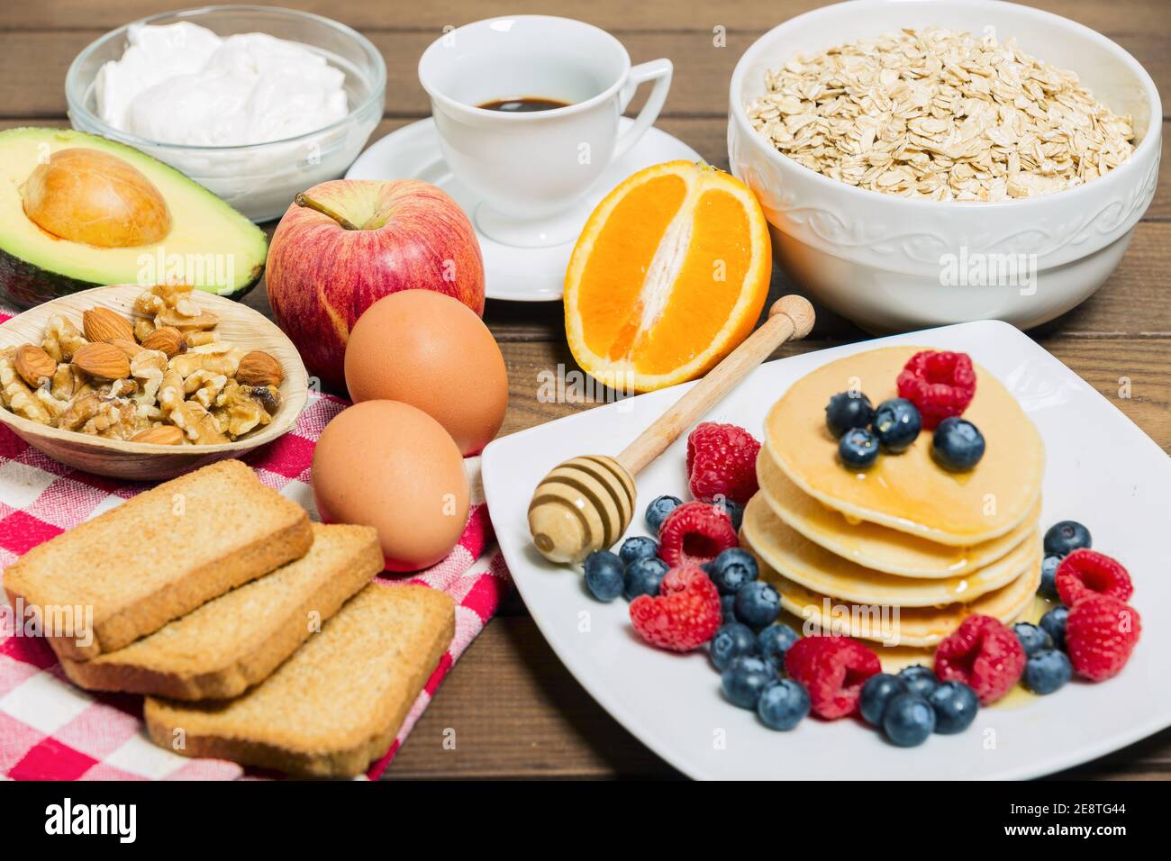 Un petit déjeuner sain avec du café, des crêpes, des baies fraîches, des œufs, de l'avocat, du yaourt grec, de l'avoine, des roussettes et de l'orange. Banque D'Images