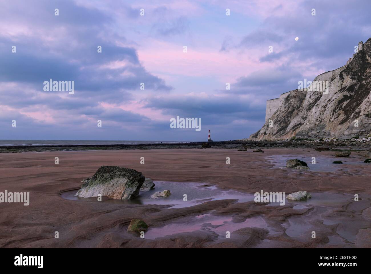 La lune de l'aube se dresse à marée basse près du phare À Beachy Head East Sussex sud-est de l'Angleterre Banque D'Images