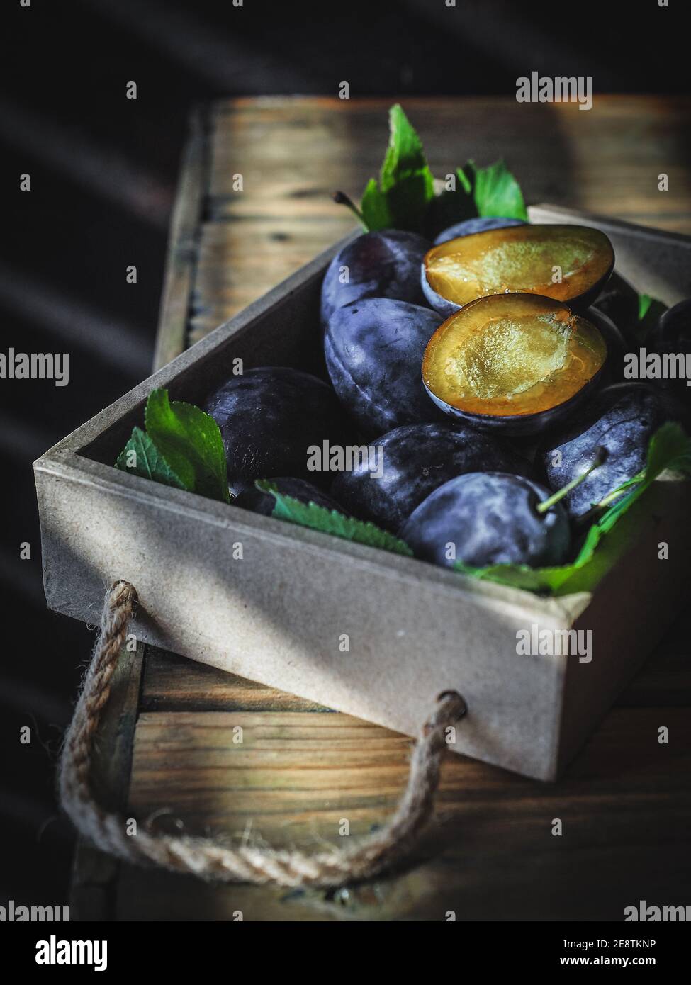 Prunes fraîchement récoltées avec une tranchée dans une boîte en bois sur une table en bois. Copier l'espace Banque D'Images