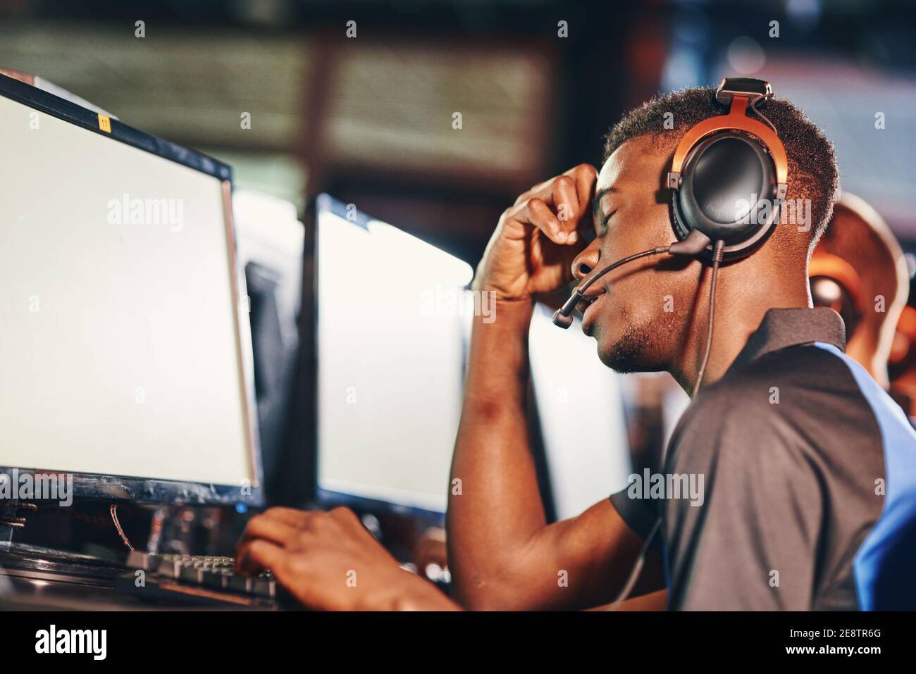 Échec. Vue latérale de mécontent africain gars, joueur professionnel de cybersport regardant l'écran de PC avec le visage triste expression tout en étant assis dans un club de jeu ou un café d'Internet. ESport Tournoi Banque D'Images