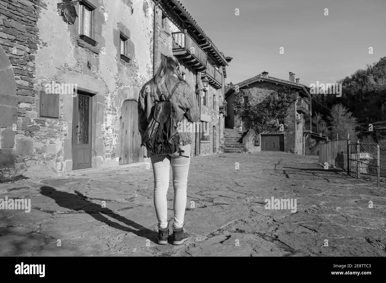 Jeune femme à la recherche de smartphone marche avec jeans de mode veste et sac à dos.Tourist concept de voyage dans le vieux village médiéval de Rupit, Barcelone, Banque D'Images