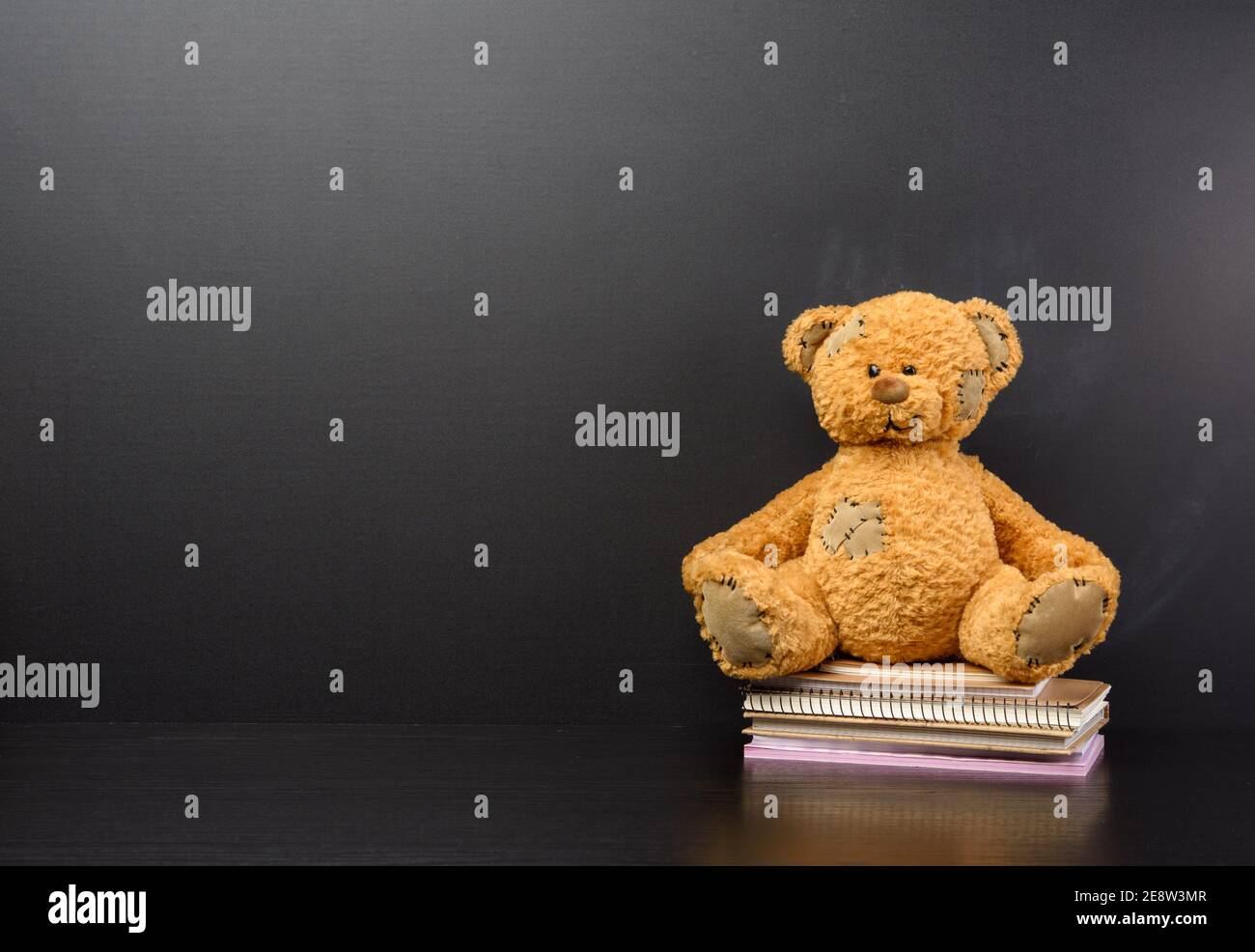 l'ours en peluche brun est assis sur une table en bois brun, derrière un tableau noir vide, de retour à l'école, un espace de copie Banque D'Images
