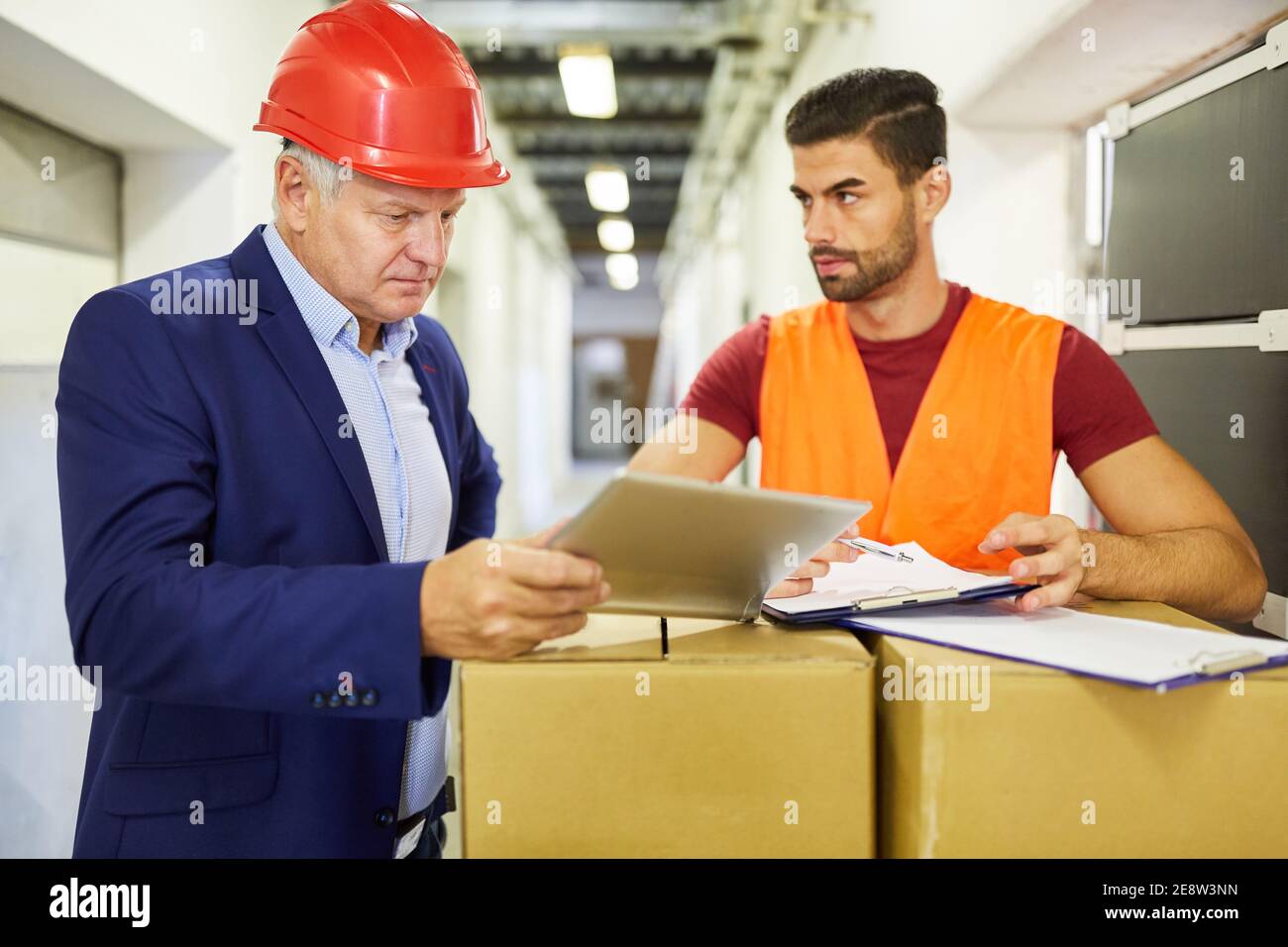 Le préposé à l'entrepôt et le patron vérifient la livraison des marchandises avec Une liste de contrôle et un PC Banque D'Images