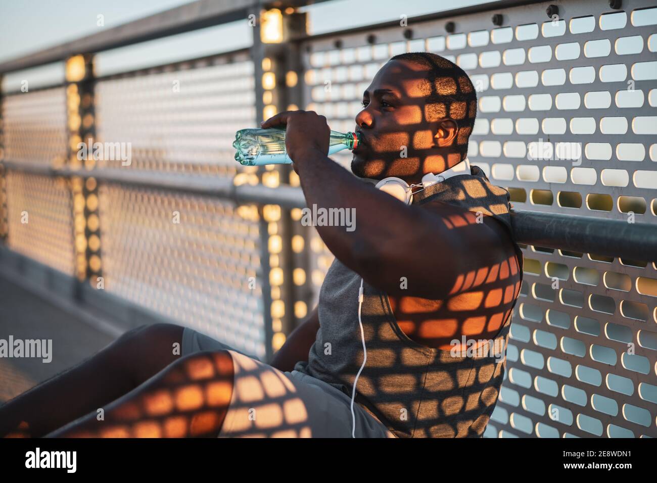 Portrait du jeune homme afro-américain en vêtements de sport qui boit de l'eau après l'exercice. Il fait de l’exercice pour réduire son poids. Banque D'Images