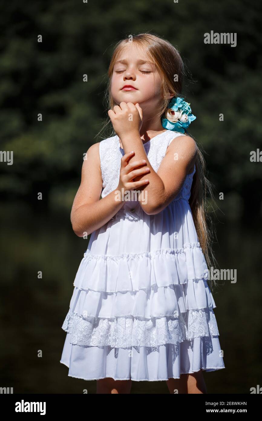 Petite fille mignonne de 6 ou 7 ans avec de longs cheveux blonds, elle est  habillée dans une robe d'été de ballet, elle est debout sur le fond de la  rivière Photo