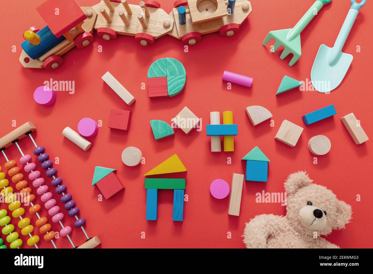 Jouets pour enfants, blocs de bois, teddy et abacus, jeu créatif pour enfants d'âge préscolaire. Arrière-plan de couleur rouge, vue de dessus. Banque D'Images