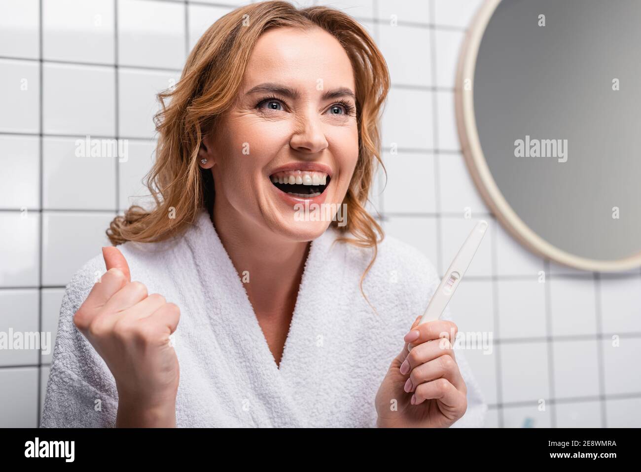 femme excitée en peignoir blanc tenant un test de grossesse dans la salle  de bains Photo Stock - Alamy
