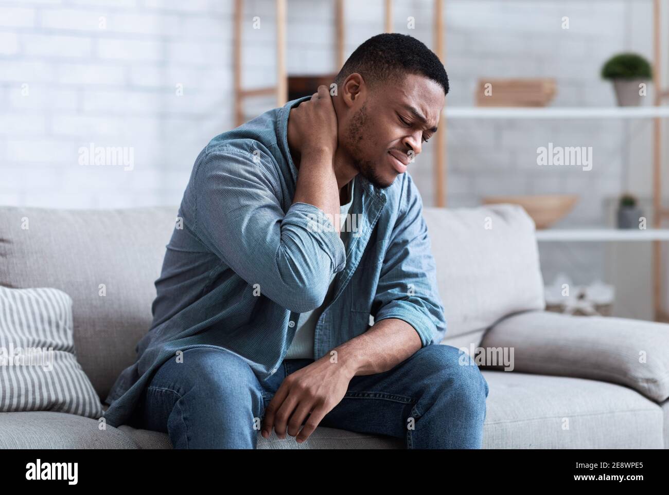 Homme noir souffrant de douleurs au cou assis sur la table à l'intérieur Banque D'Images