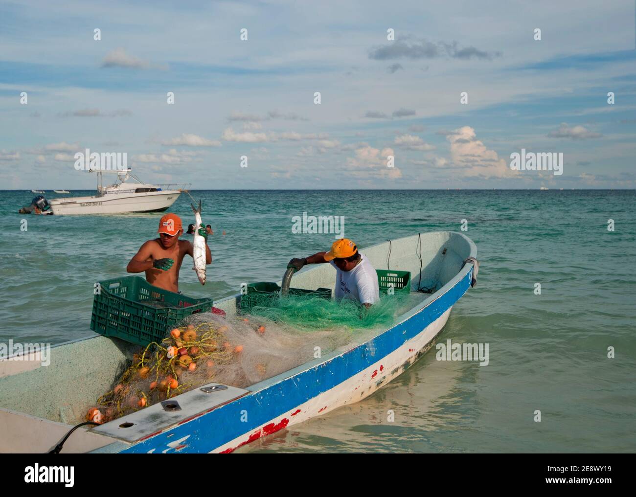 Deux jeunes pêcheurs sur leur bateau avec des filets de pêche remplissent les caisses de poissons. En arrière-plan la mer des Caraïbes et le ciel nuageux. Mexique Banque D'Images