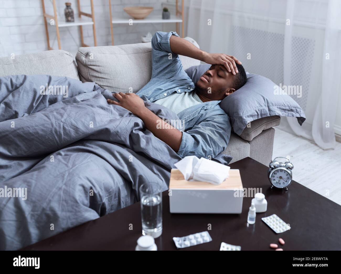 Homme noir malade ayant de la fièvre couché sur un canapé à la maison Banque D'Images