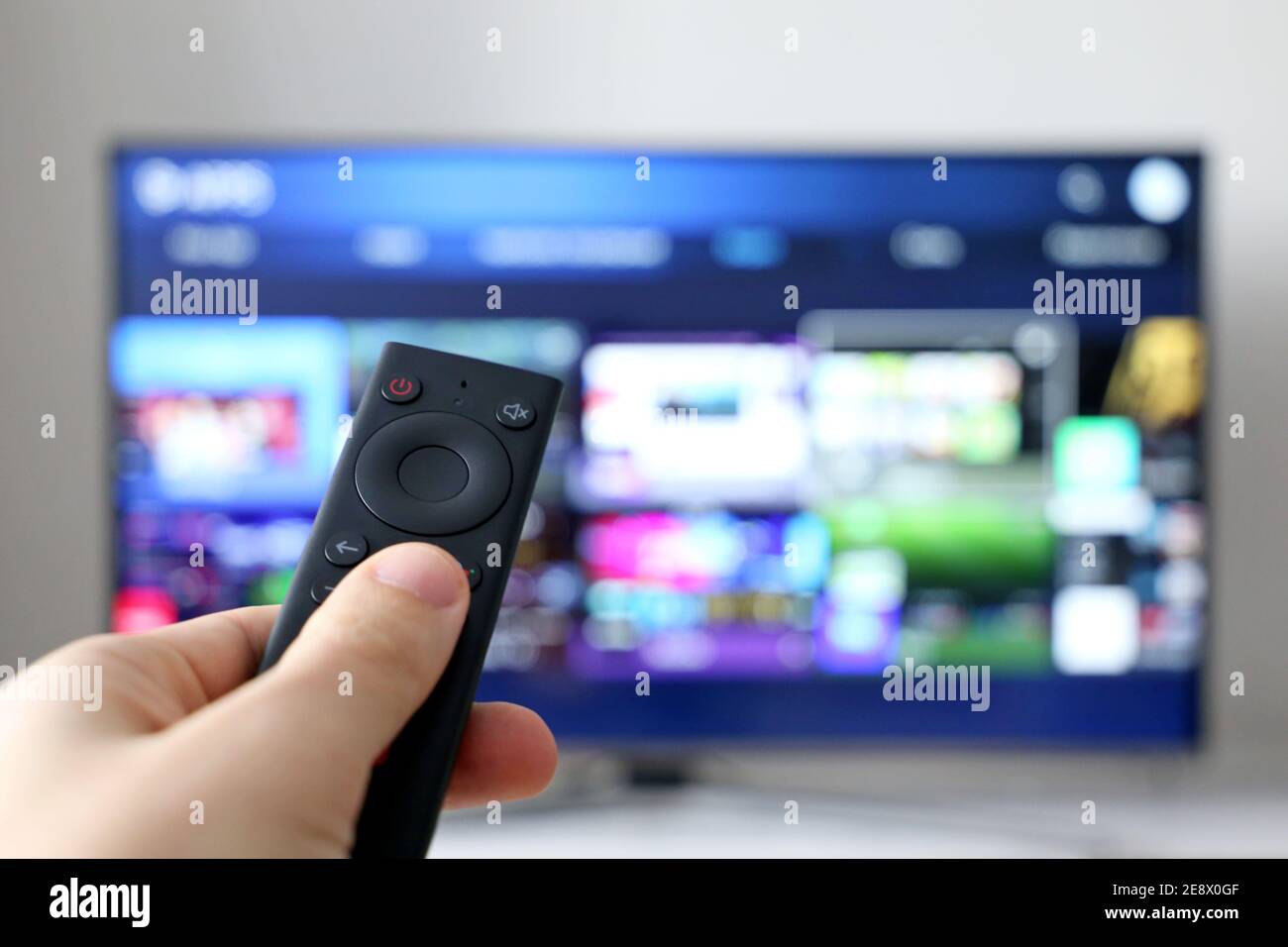 Main mâle avec télécommande sur l'arrière-plan de l'écran Smart TV. Personne choisissant des services de streaming, regardant des films Banque D'Images