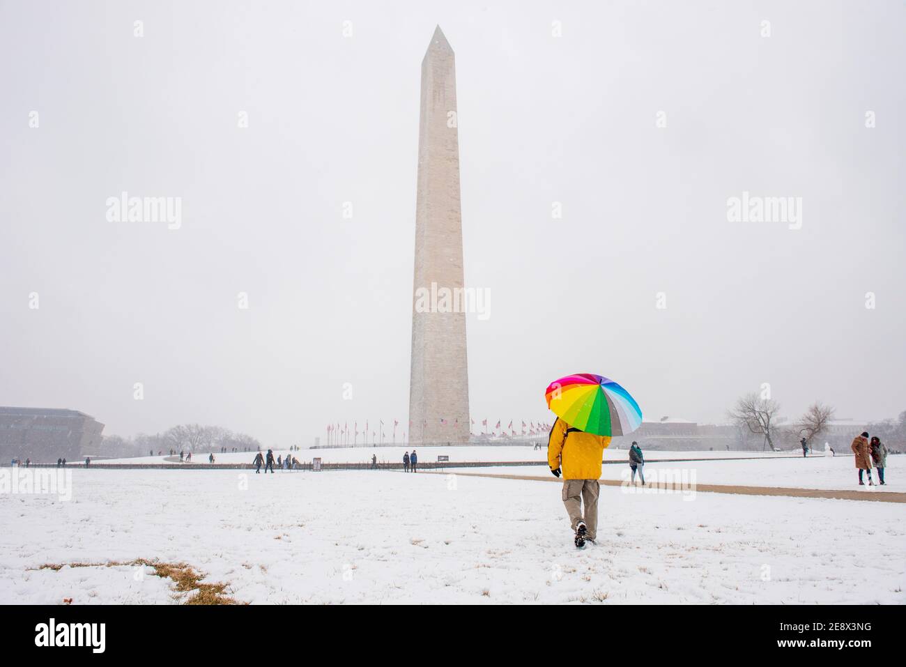 Un homme porte un parapluie coloré pendant une journée enneigée sur le National Mall à Washington, D.C. le Washignton Monument peut être vu au loin. Banque D'Images