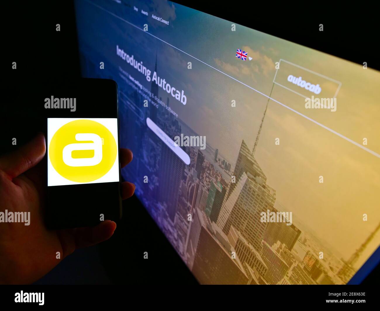 Personne tenant un téléphone portable avec le logo de la société britannique de développement de logiciel de taxi Autocolab Ltd sur l'affichage en face de la page Web. Mise au point sur l'écran du téléphone. Banque D'Images