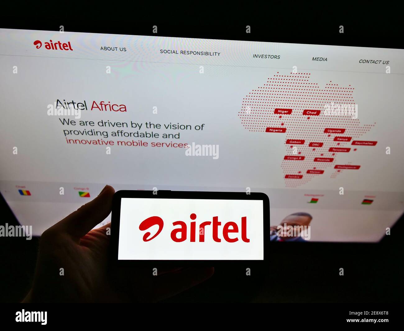 Personne portant un smartphone avec le logo du fournisseur de télécommunications Airtel Africa plc exposé devant le site Web. Mise au point sur l'écran du téléphone mobile. Banque D'Images