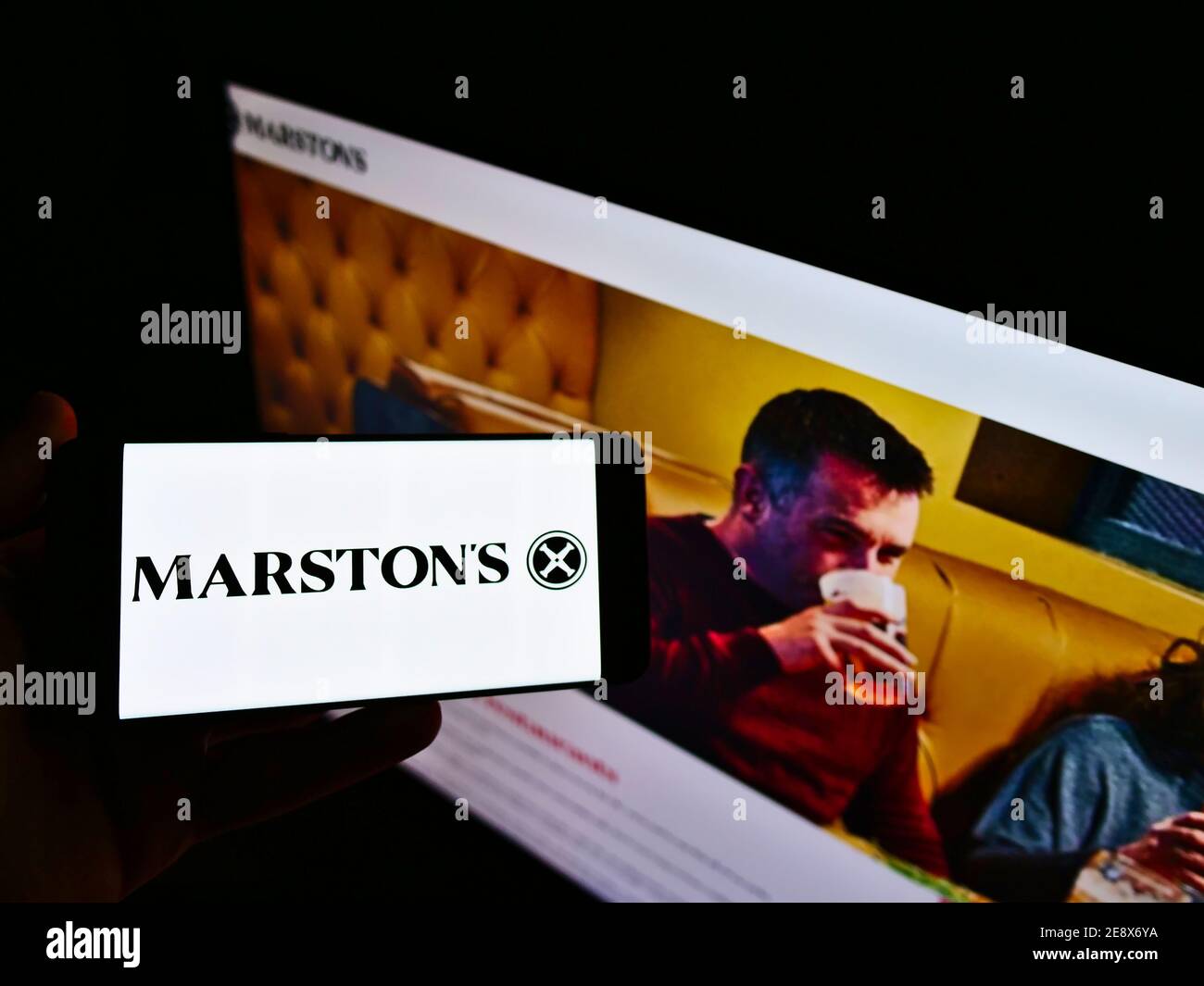 Vue en grand angle de la personne qui tient un téléphone portable avec le logo de la brasserie britannique, de l'hôtel et de l'opérateur de pub Marston's plc. Mise au point sur l'écran du téléphone. Banque D'Images