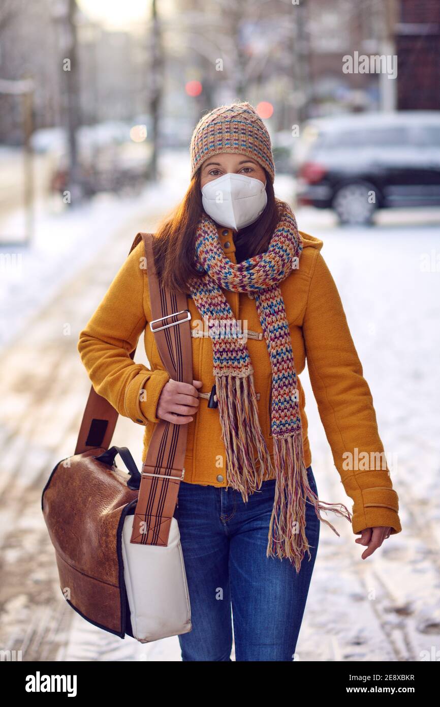 Femme brune d'âge moyen en vêtements d'hiver portant un masque facial à l'extérieur En raison du virus Corona dehors pendant son chemin à travail Banque D'Images
