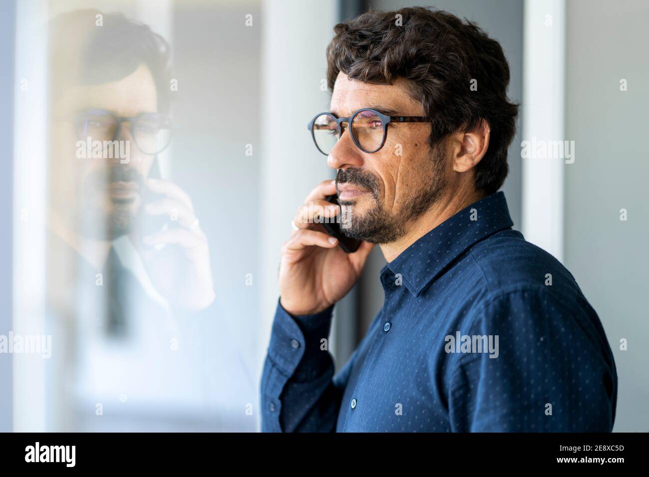 Homme décontracté portant des lunettes pour passer un appel téléphonique. Portrait réussi de l'homme au bureau près de la fenêtre Banque D'Images
