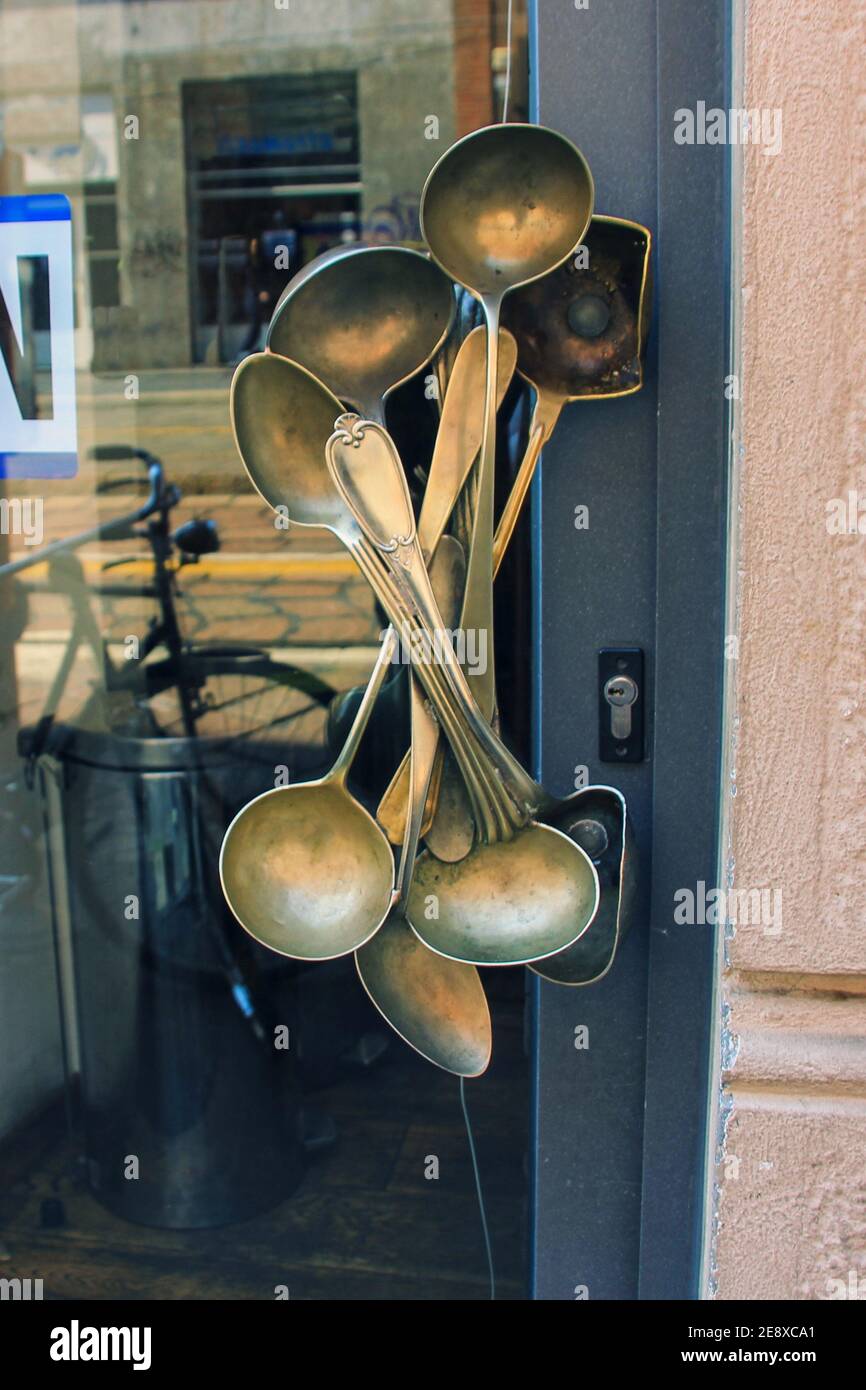 Poignée de porte en laiton vintage conçue à partir de grandes cuillères vieillies, pelles sur porte en verre avec réflexion floue devant le café de bistro. Banque D'Images
