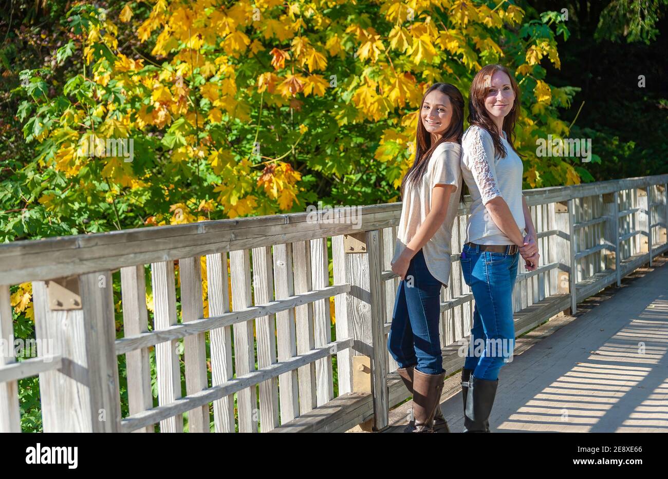 Mère et fille posent sur un pont avec des feuilles d'automne en arrière-plan. Banque D'Images