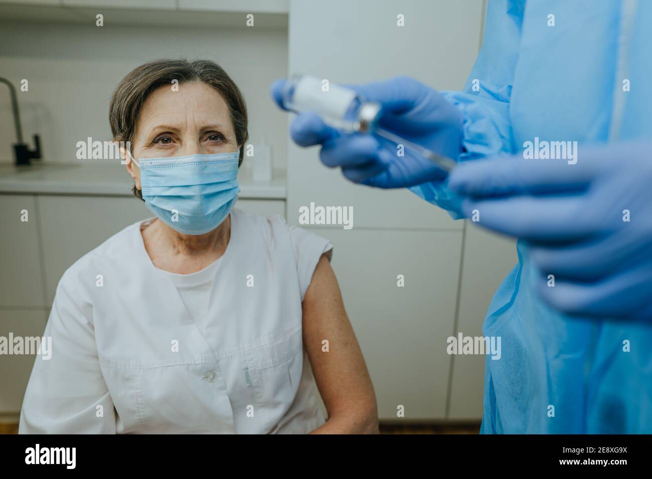 Femme mature travailleuse de soins de santé attendant la vaccination COVID-19 à l'hôpital. Médecin dans l'ensemble de protection et les gants tenant le vaccin et la seringue dans le TH Banque D'Images