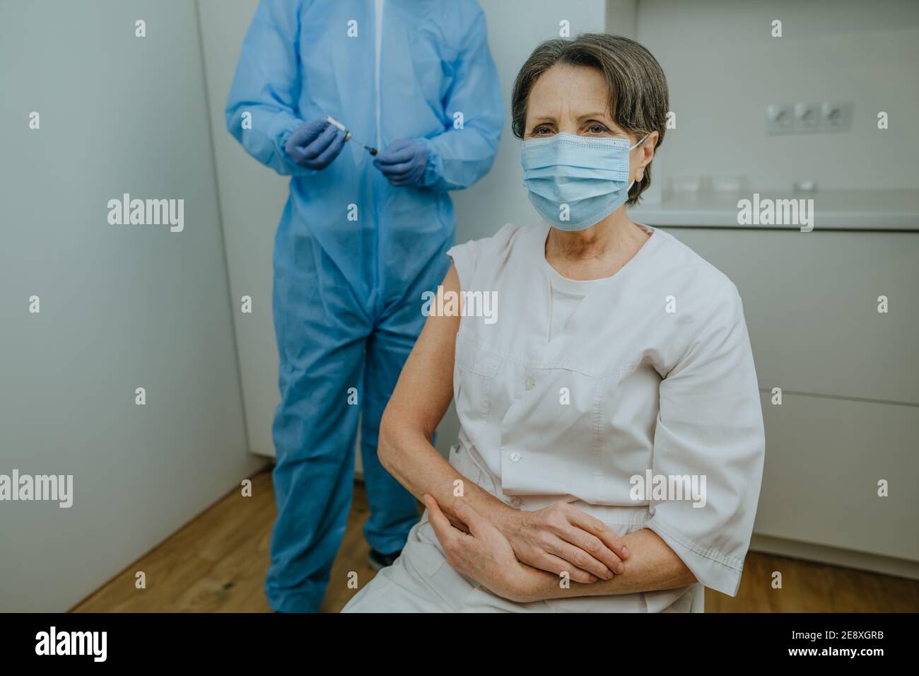 Femme mature travailleuse de soins de santé attendant la vaccination COVID-19 à l'hôpital. Médecin dans l'ensemble de protection et les gants tenant le vaccin et la seringue dans le TH Banque D'Images