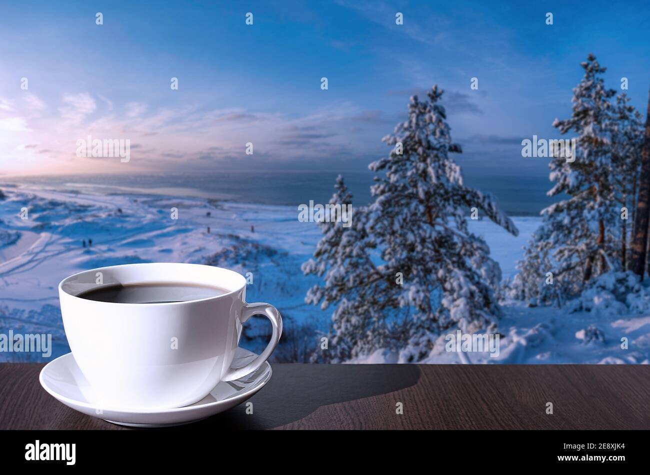 Tasse de café sur la table avec vue sur la plage enneigée avec dunes, mer Baltique et couvert de sapins de neige sur la colline. Banque D'Images