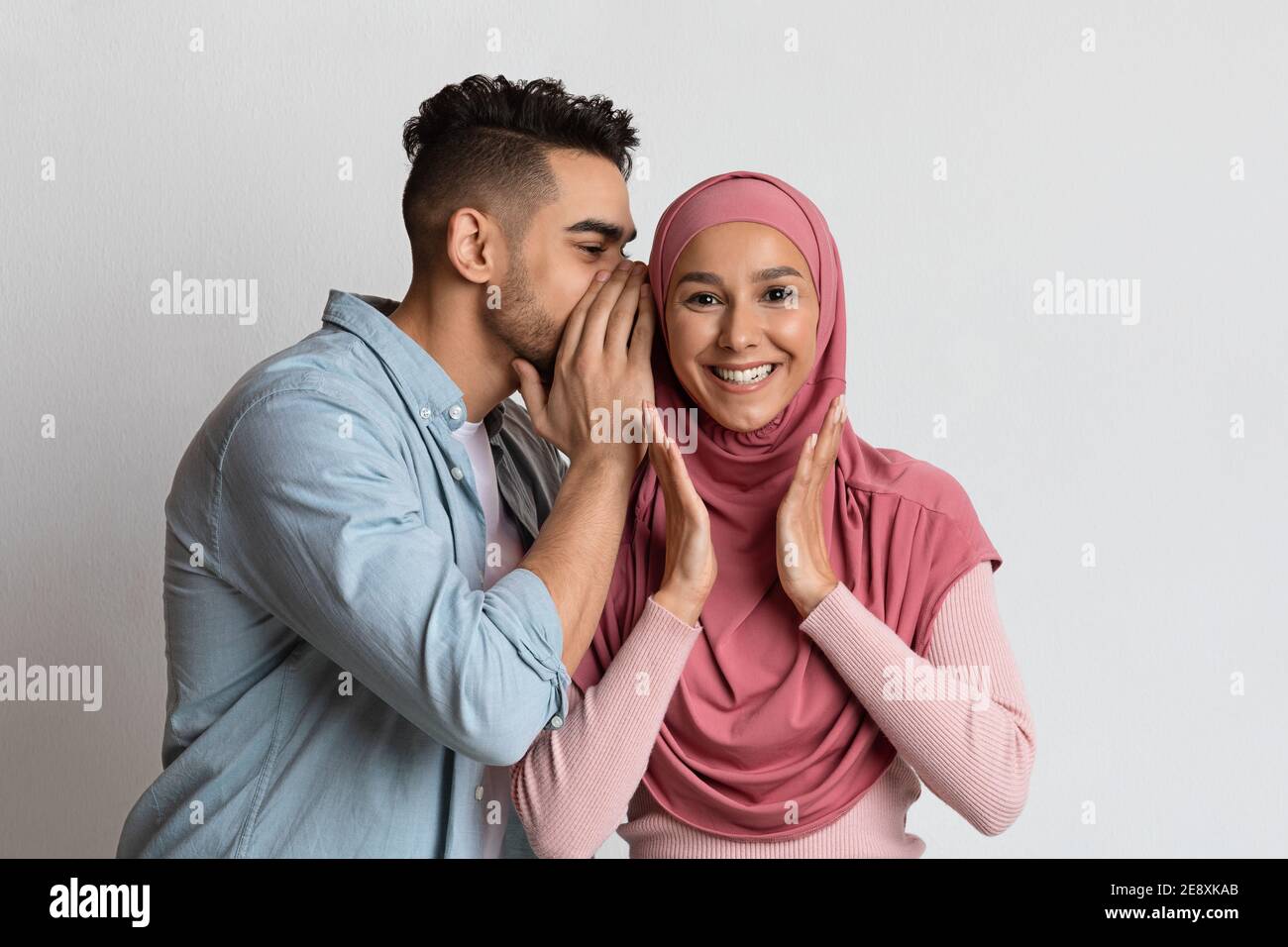 Gossips concept. Un homme arabe joyeux chuchote quelque chose dans l'oreille de sa petite amie musulmane Banque D'Images
