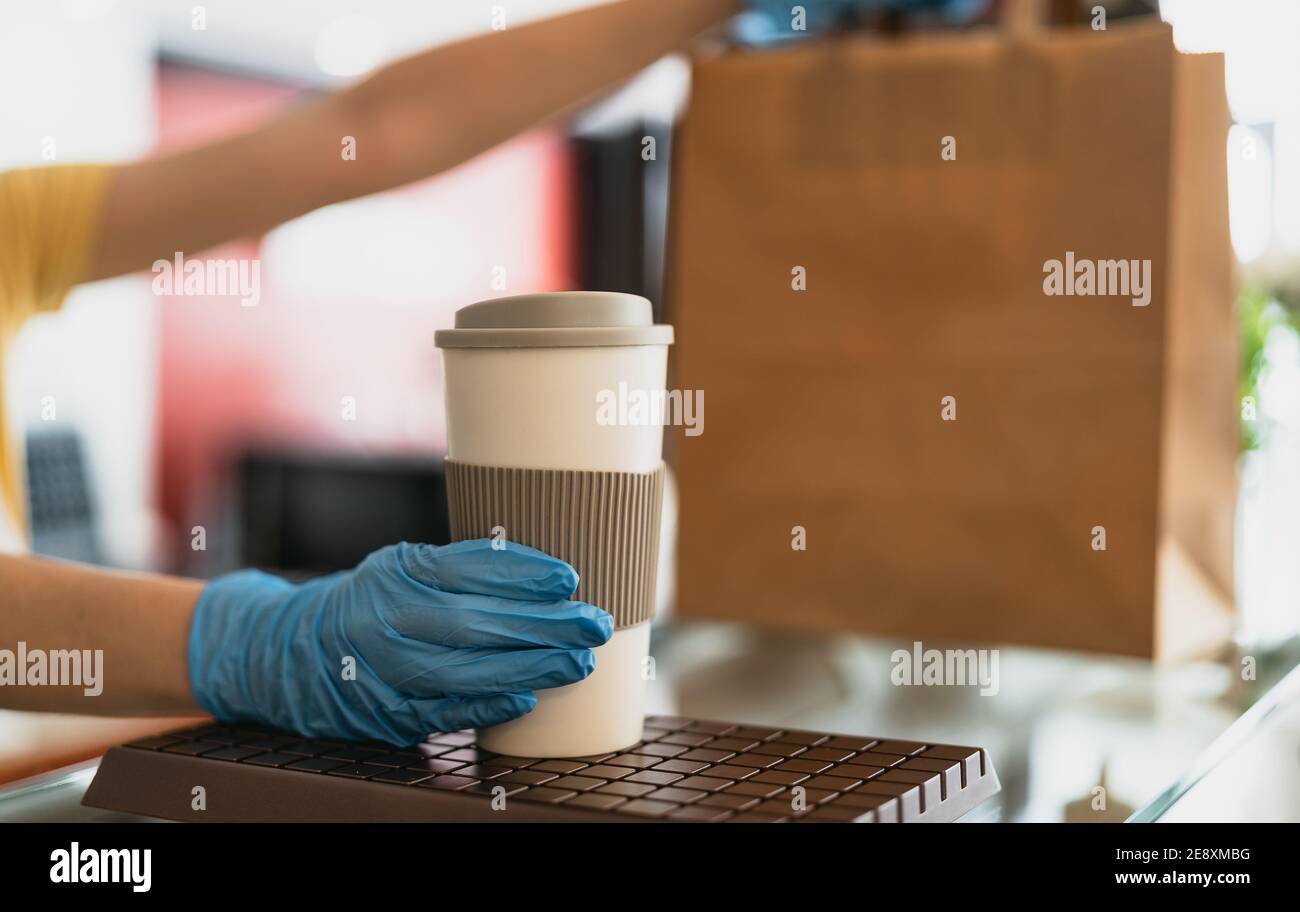 Le propriétaire du bar ne travaille qu'avec les commandes à emporter pendant la période corona Éclosion de virus - jeune femme travailleuse portant des gants chirurgicaux donnant repas à emporter et café Banque D'Images