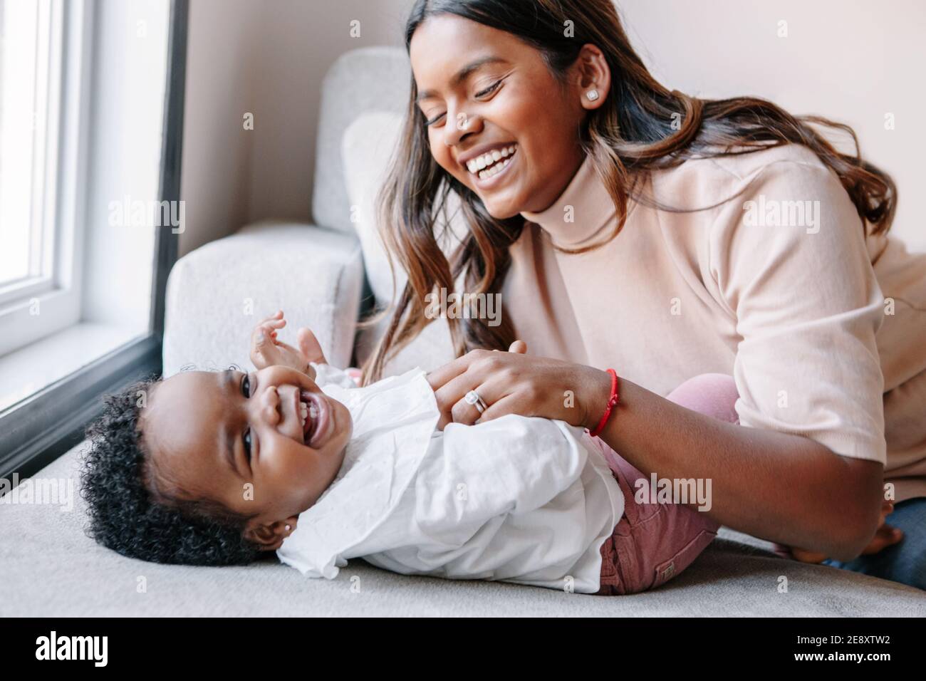 Joyeux sourire riant mere indienne jouant avec fille noire de bebe fille. La famille a melange les gens de course maman et enfant ensemble se serrant a la maison. Authentique c Photo