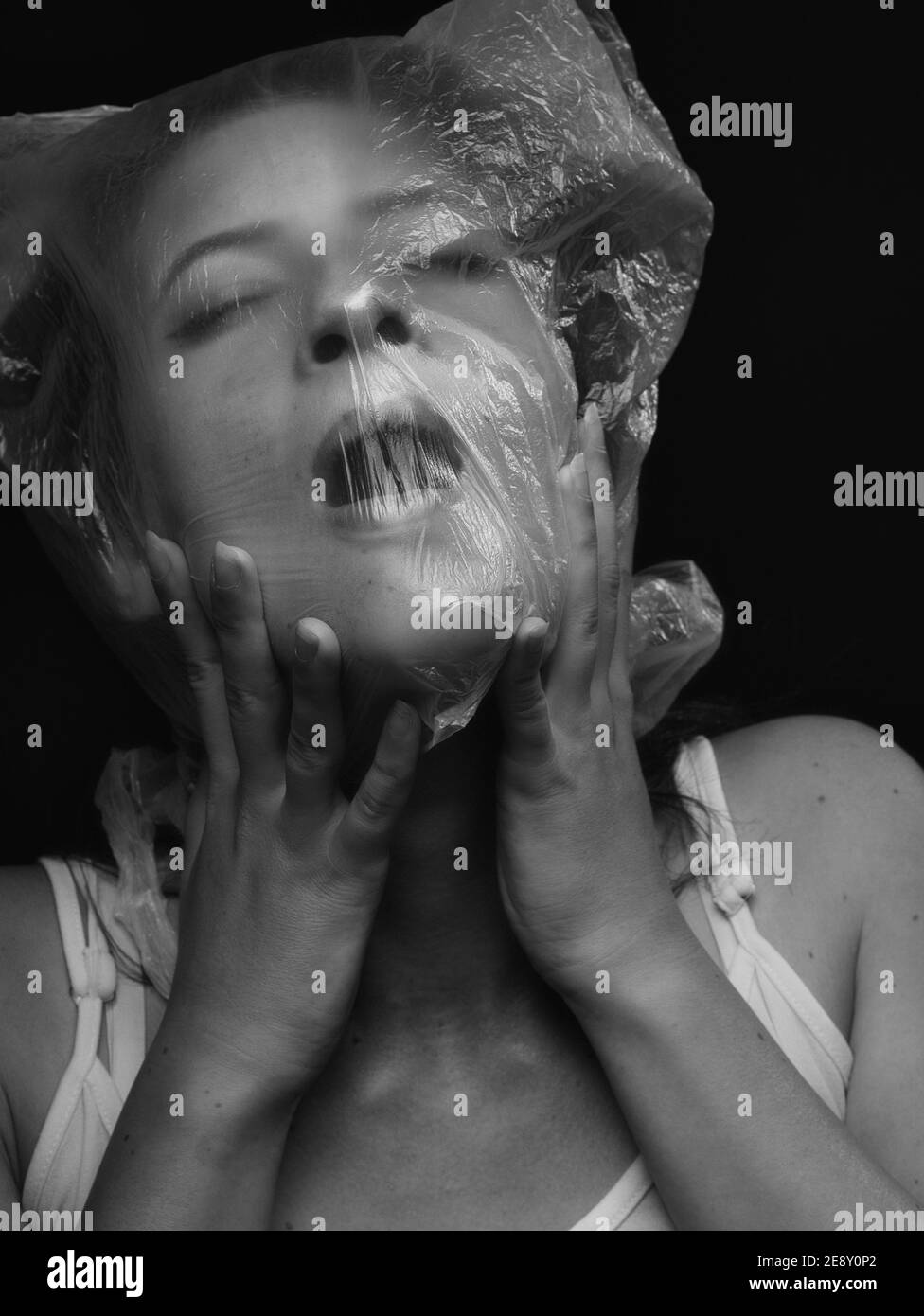 une jeune femme visage, chaussant sur sac plastique. atmosphère sombre, fond noir. Banque D'Images